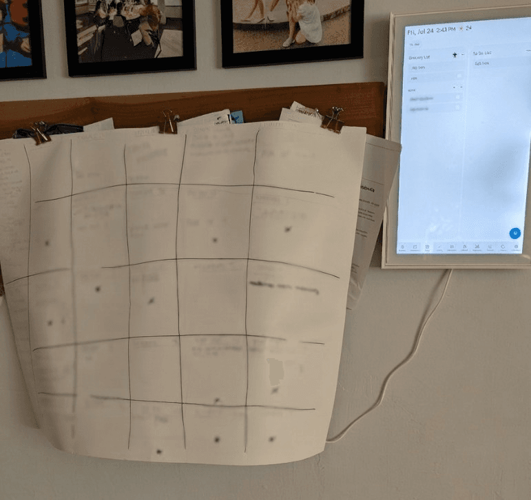 A hand-drawn posterboard calendar hanging next to a wall-mounted smart family calendar display in a kitchen